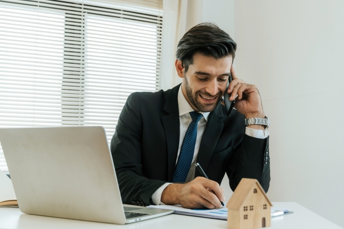 A businessman on the phone next to a wooden model of a house