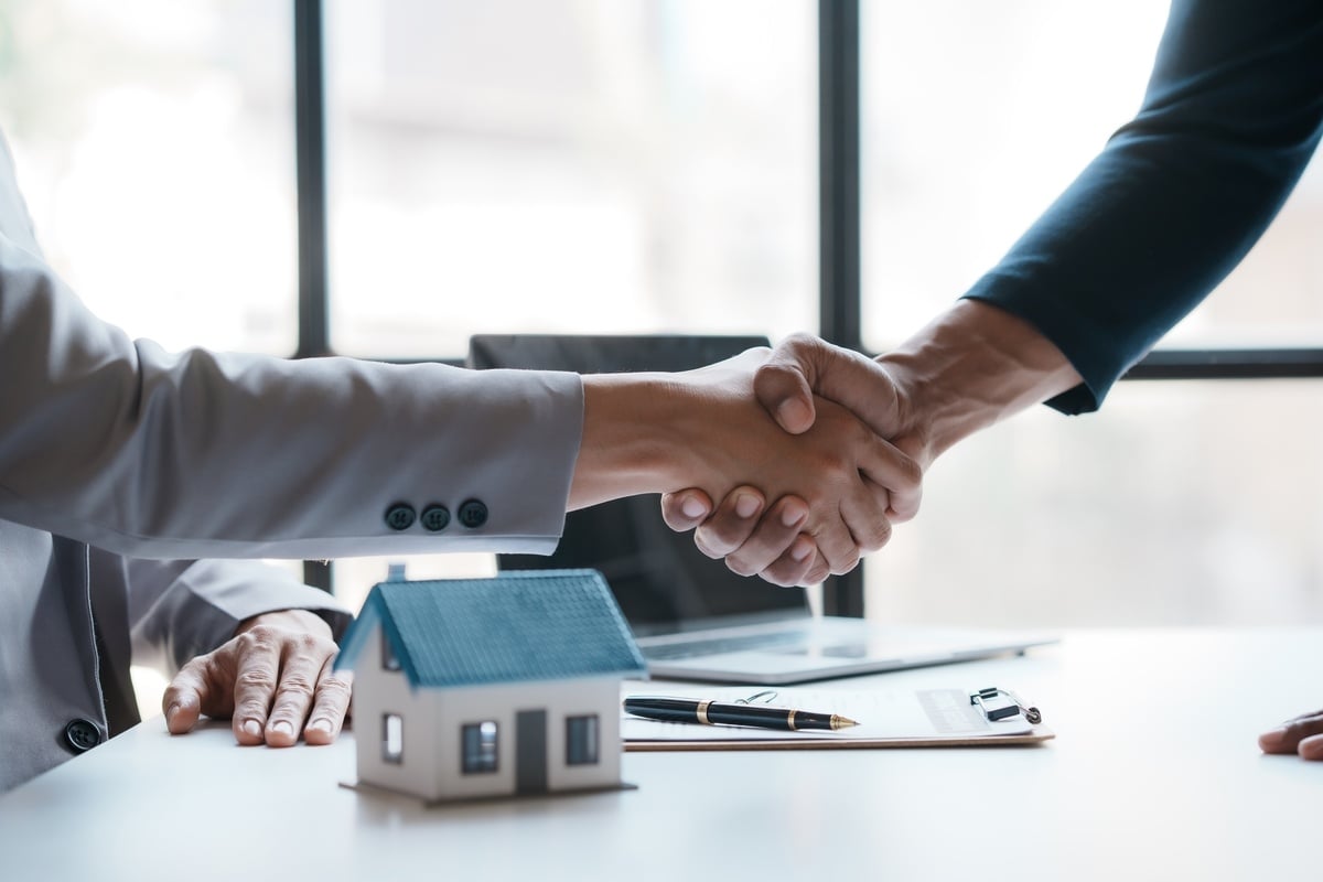 Two people shaking hands next to a model house