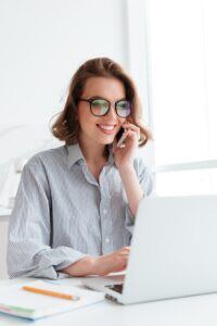close-up-portrait-happy-young-woman-striped-shirt-talking-smartphone-while-using-laptop-computer-home-min-200x300